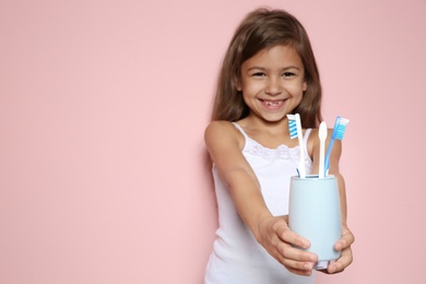 Photo of Portrait of little girl holding cup with toothbrushes on color background. Space for text