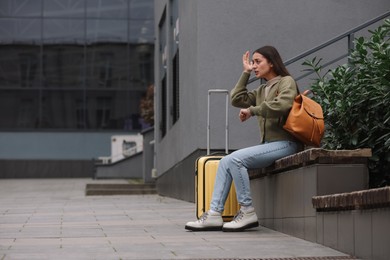 Photo of Being late. Worried woman with suitcase sitting on bench outdoors, space for text