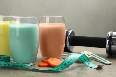 Photo of Tasty shakes, dumbbell, measuring tape and pieces of carrot on gray table, closeup. Weight loss