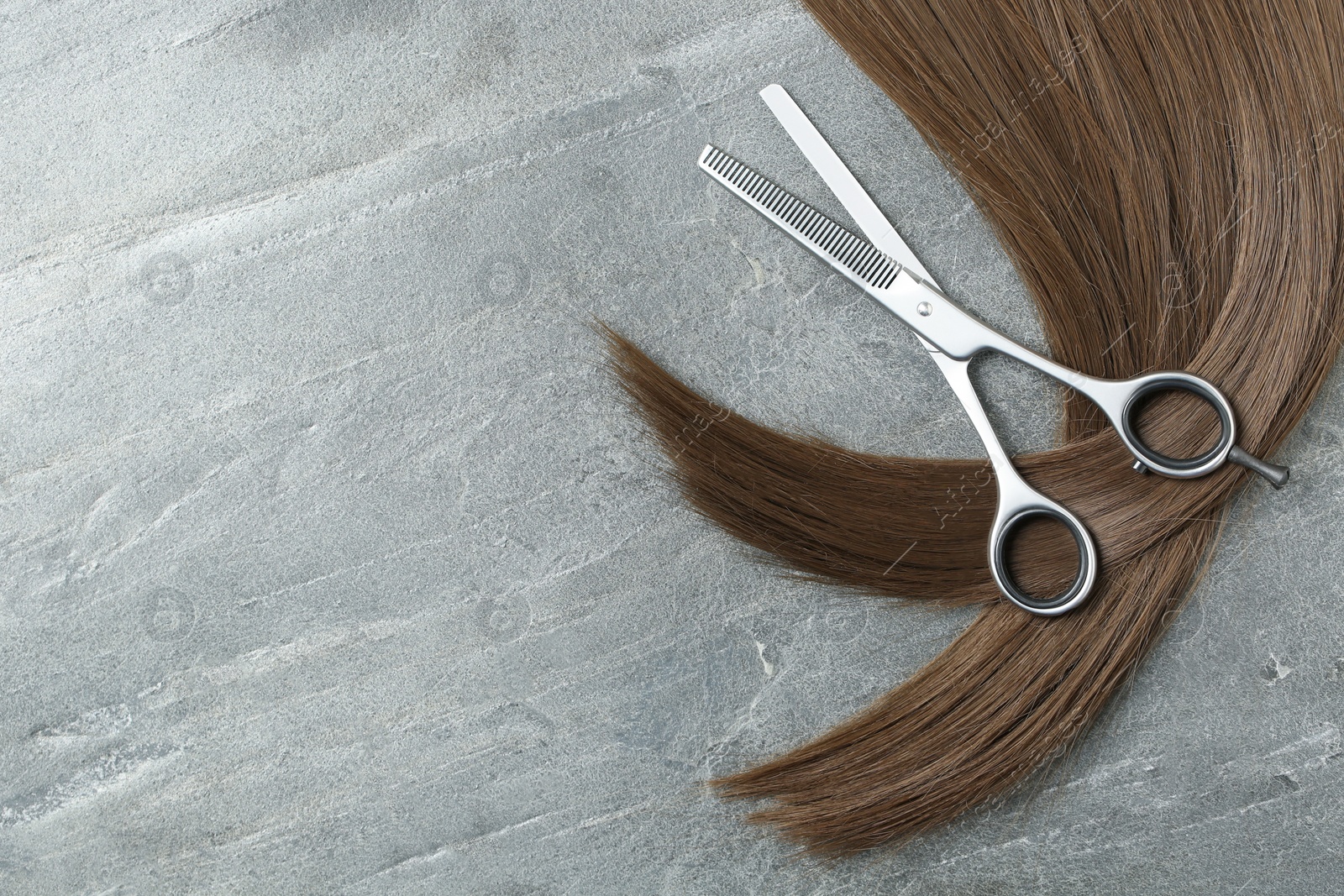 Photo of Flat lay composition with brown hair, thinning scissors and space for text on grey background. Hairdresser service