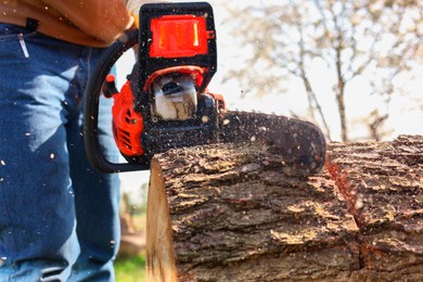 Man sawing wooden log outdoors, closeup view