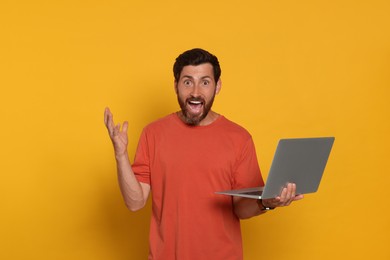 Emotional man with laptop on orange background