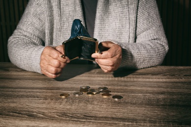 Photo of Poor senior woman with empty wallet and coins at table, closeup