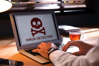 Photo of Man using laptop with warning about virus attack at workplace, closeup