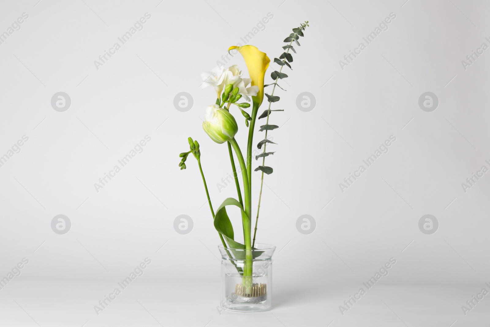 Photo of Beautiful ikebana for stylish house decor. Floral composition with fresh flowers and eucalyptus branch on white background