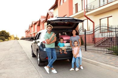 Photo of Happy family with suitcases near car in city street