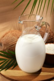 Photo of Glass jug of delicious vegan milk near coconuts on brown background