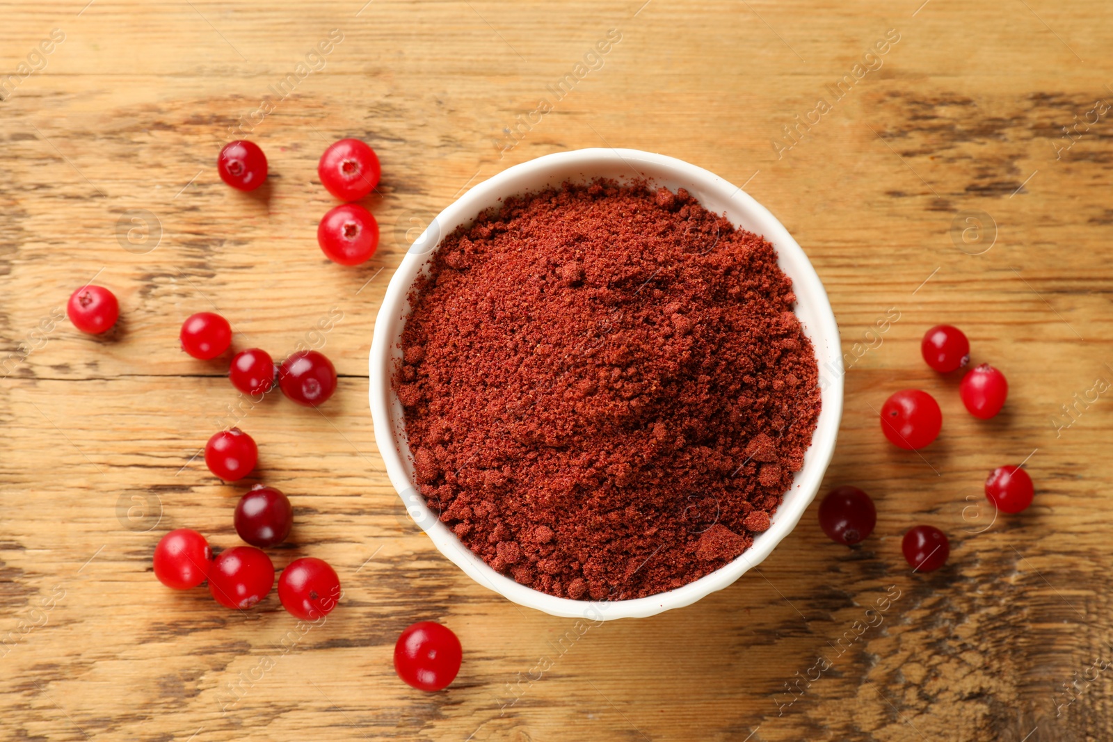 Photo of Dried cranberry powder in bowl and fresh berries on wooden table, top view