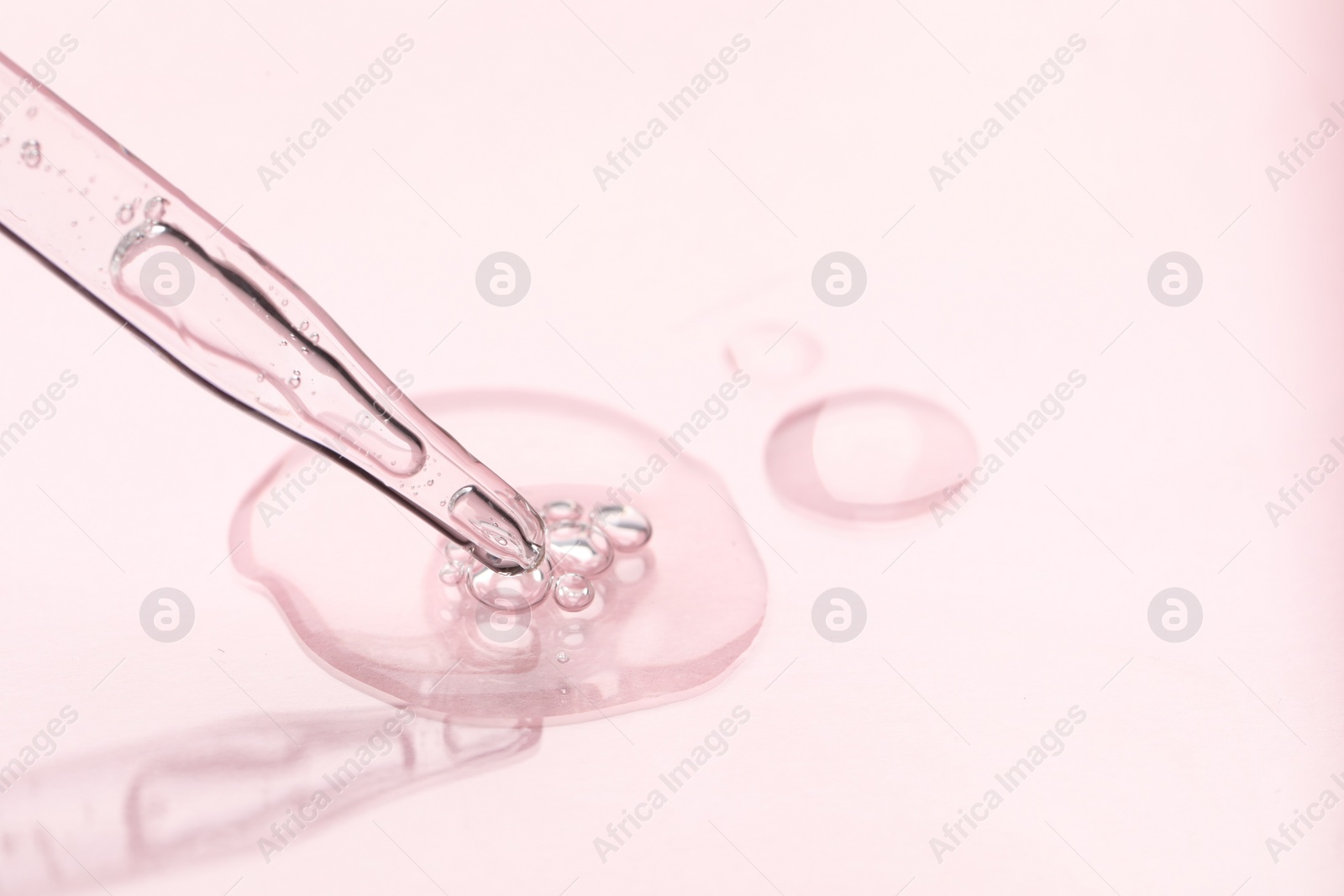 Photo of Glass pipette and transparent liquid on light pink background, closeup. Space for text