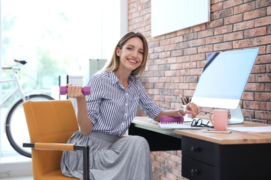 Photo of Beautiful businesswoman lifting weights in office. Workplace fitness