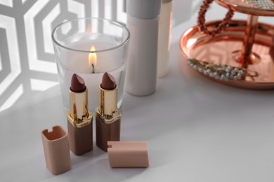 Photo of Burning soy candle and lipsticks on white table indoors