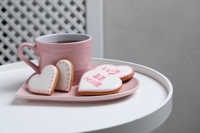 Photo of Delicious heart shaped cookies and cup of tea on white table