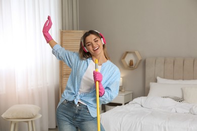 Photo of Woman in headphones with mop singing while cleaning at home