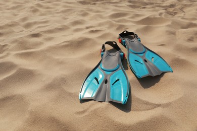 Photo of Pair of turquoise flippers on sand. Space for text
