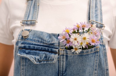 Photo of Woman with beautiful tender flowers in denim jumpsuit's pocket, closeup