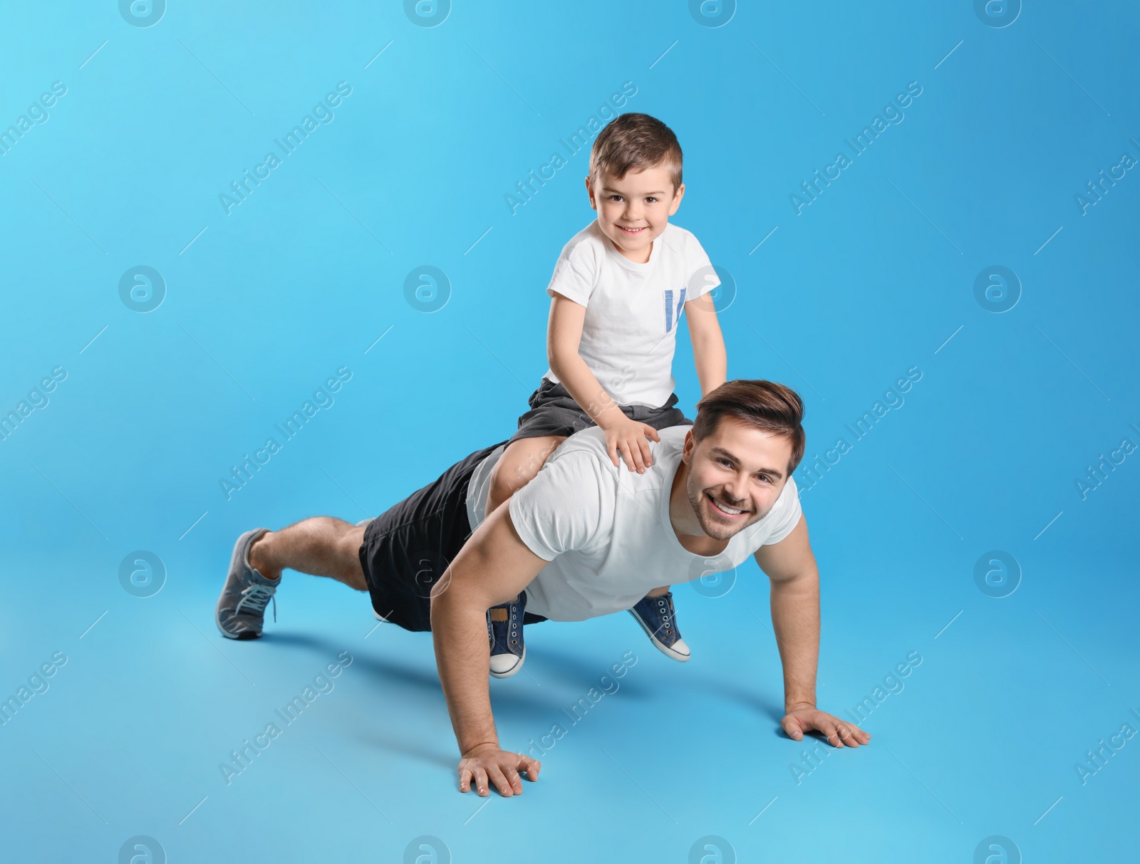 Photo of Dad doing push-ups with son on his back against color background