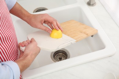 Photo of Man rubbing cutting board with lemon at sink in kitchen, closeup
