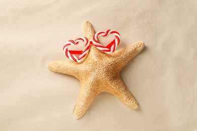 Photo of Beautiful starfish with candy cane party sunglasses on sand, top view. Christmas vacation