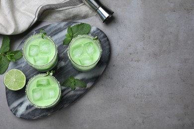 Photo of Delicious mint liqueur with ice cubes and green leaves on grey table, flat lay. Space for text