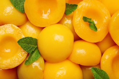 Halves of canned peaches with mint leaves as background, top view
