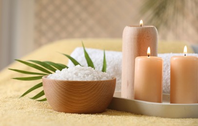 Photo of Spa composition. Burning candles, sea salt and towel on soft yellow surface