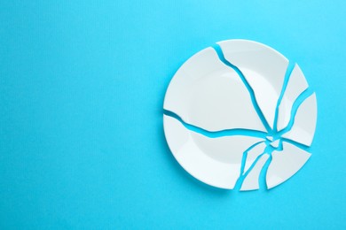 Photo of Pieces of broken ceramic plate on light blue background, flat lay. Space for text