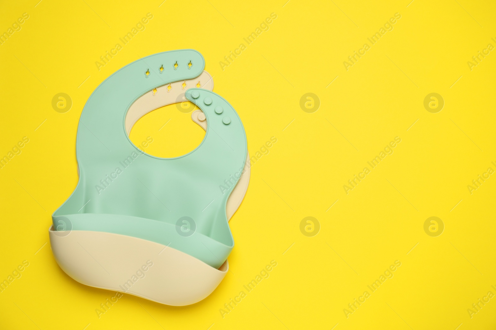 Photo of Two silicone baby bibs on yellow background, top view. Space for text