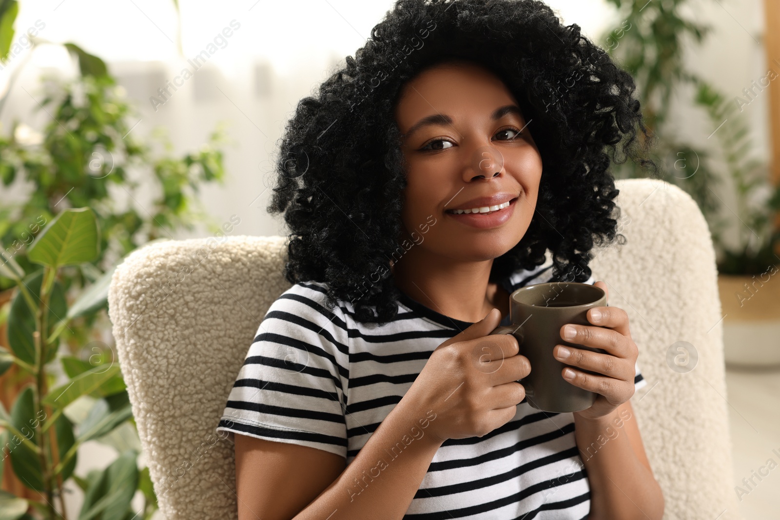 Photo of Relaxing atmosphere. Portrait of happy woman with cup of hot drink near houseplants at home