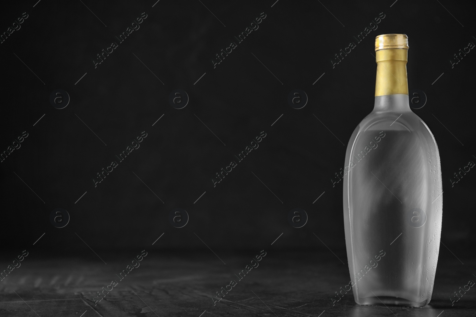 Photo of Bottle of vodka on grey table against black background. Space for text