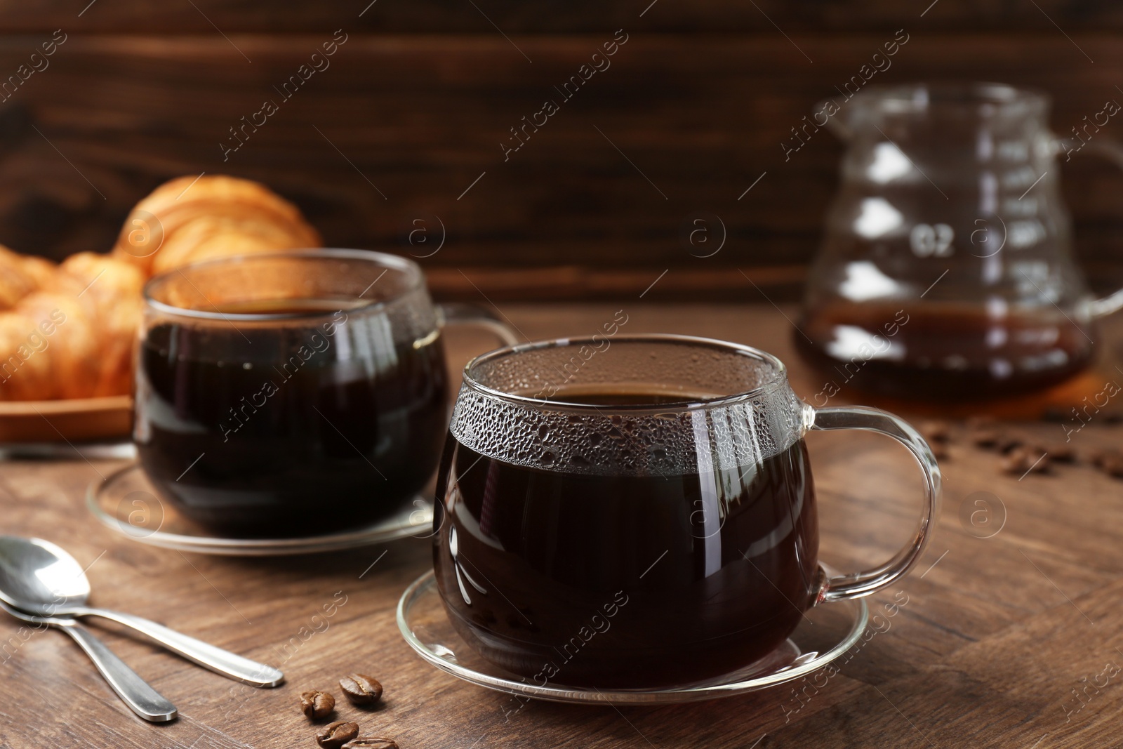 Photo of Hot coffee in glass cups, spoons and beans on wooden table, closeup