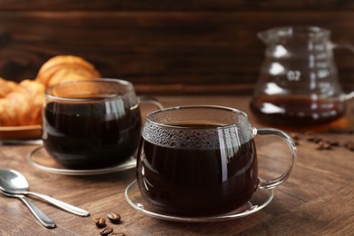 Photo of Hot coffee in glass cups, spoons and beans on wooden table, closeup