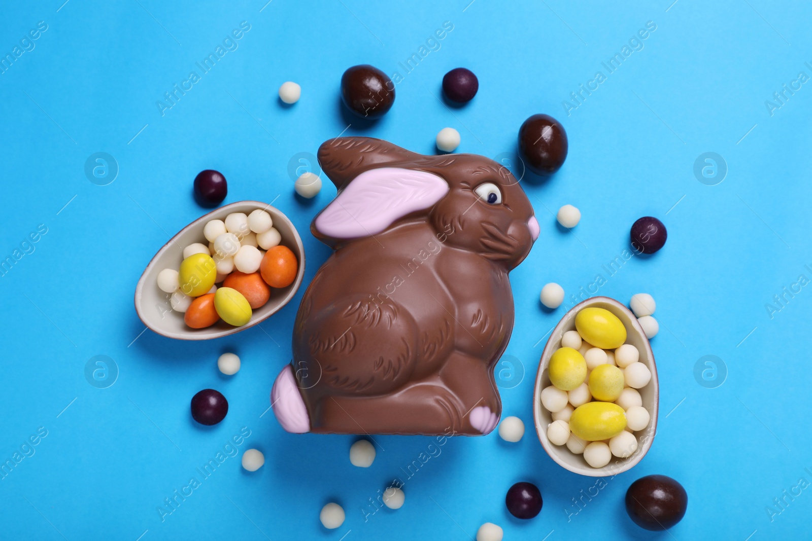 Photo of Chocolate Easter bunny, halves of egg and candies on light blue background, flat lay