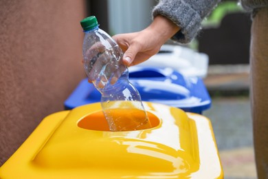Woman throwing plastic bottle into recycling bin outdoors, closeup