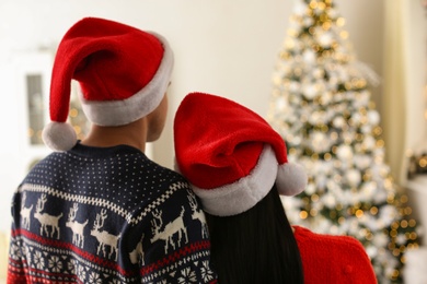 Photo of Couple in Santa hats at home, back view. Christmas celebration
