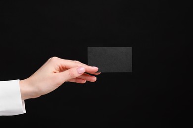 Woman holding blank business card on black background, closeup. Space for text