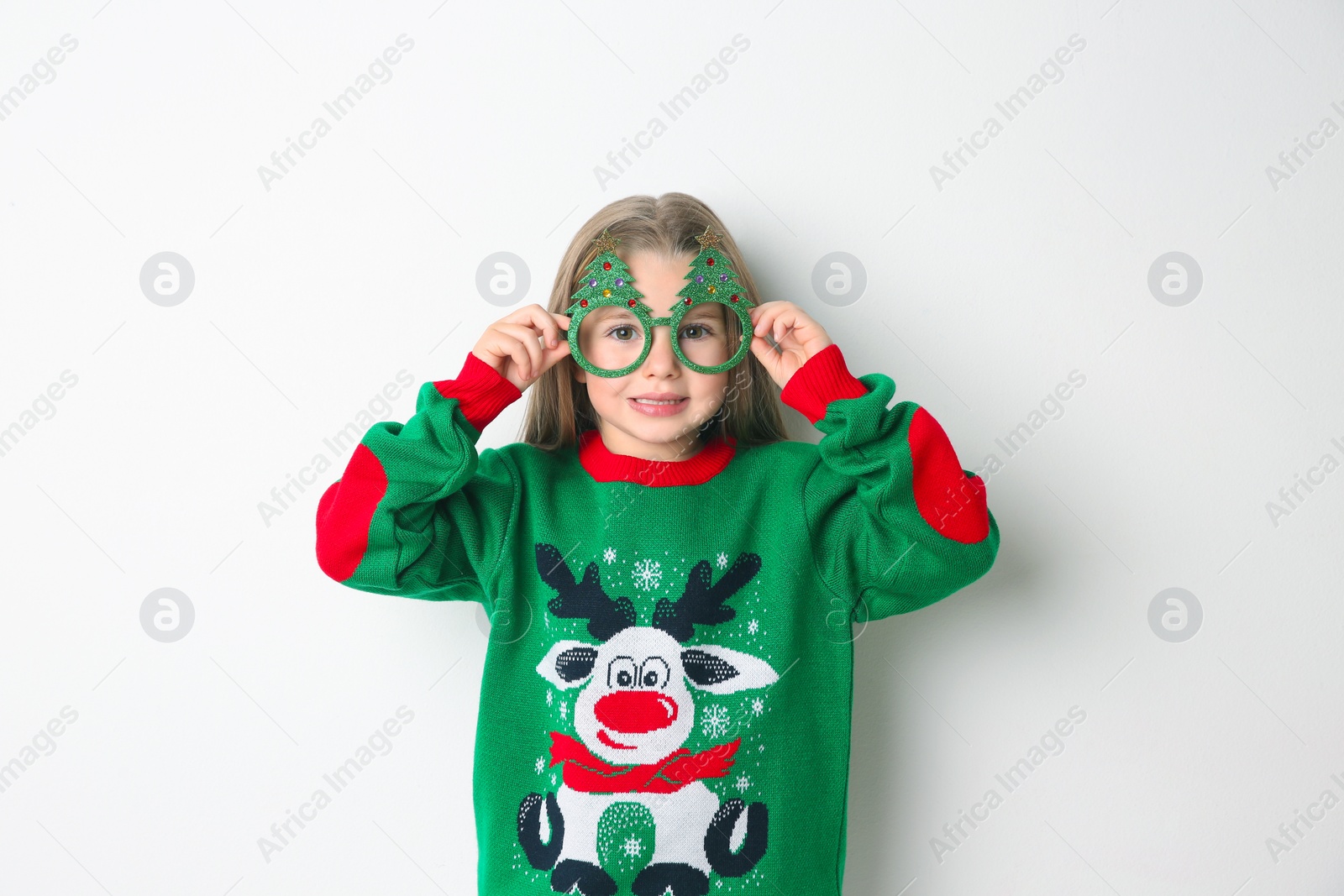 Photo of Cute little girl in Christmas sweater and party glasses on white background