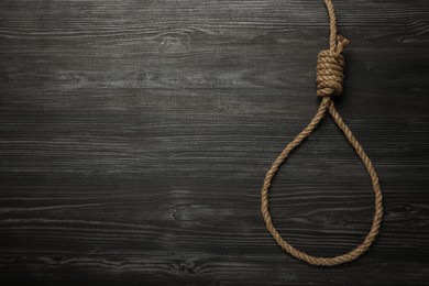 Photo of Rope noose on black wooden table, top view. Space for text