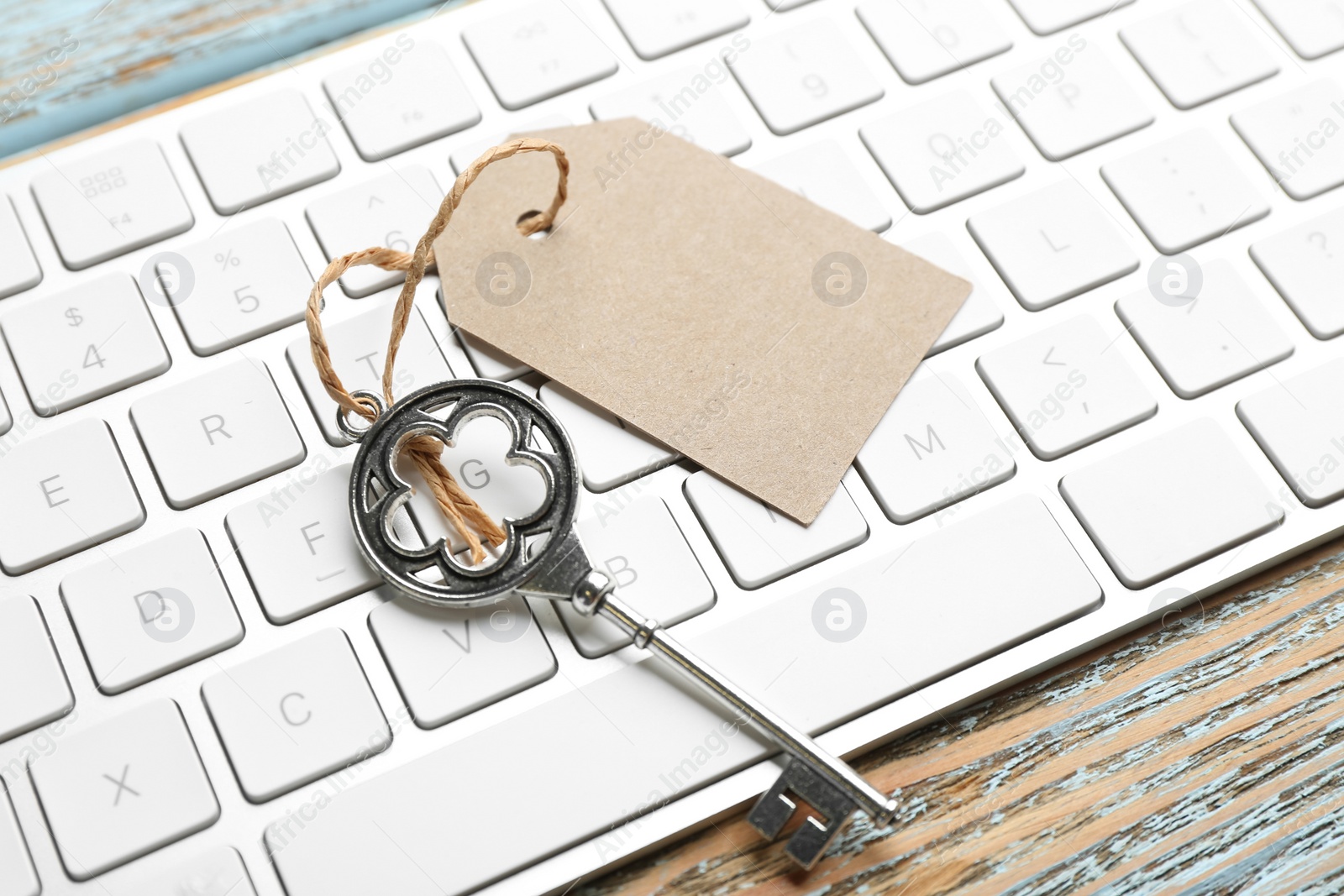 Photo of Key with blank tag and computer keyboard on wooden table, closeup. Keyword concept