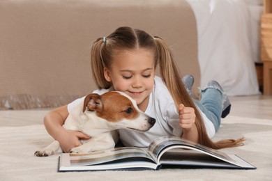Photo of Cute girl reading book on floor with her dog at home. Adorable pet