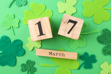 St. Patrick's day - 17th of March. Block calendar and decorative clover leaves on green background, flat lay
