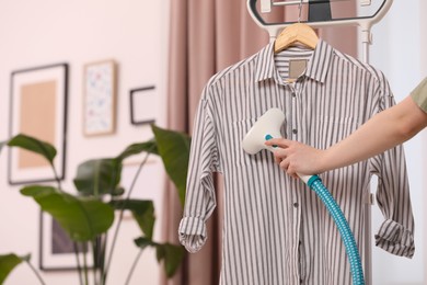 Woman steaming shirt on hanger at home, closeup. Space for text