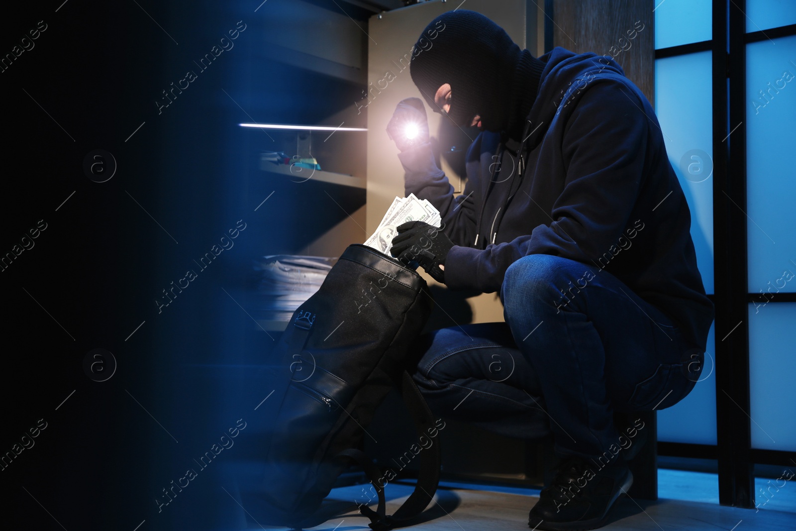 Photo of Thief taking money out of steel safe indoors at night