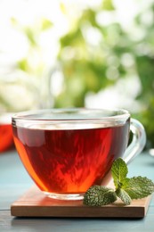 Glass cup of aromatic black tea with fresh mint on light blue wooden table against blurred background. Space for text