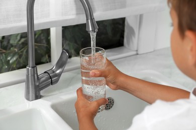 Boy filling glass with water from tap at home, closeup