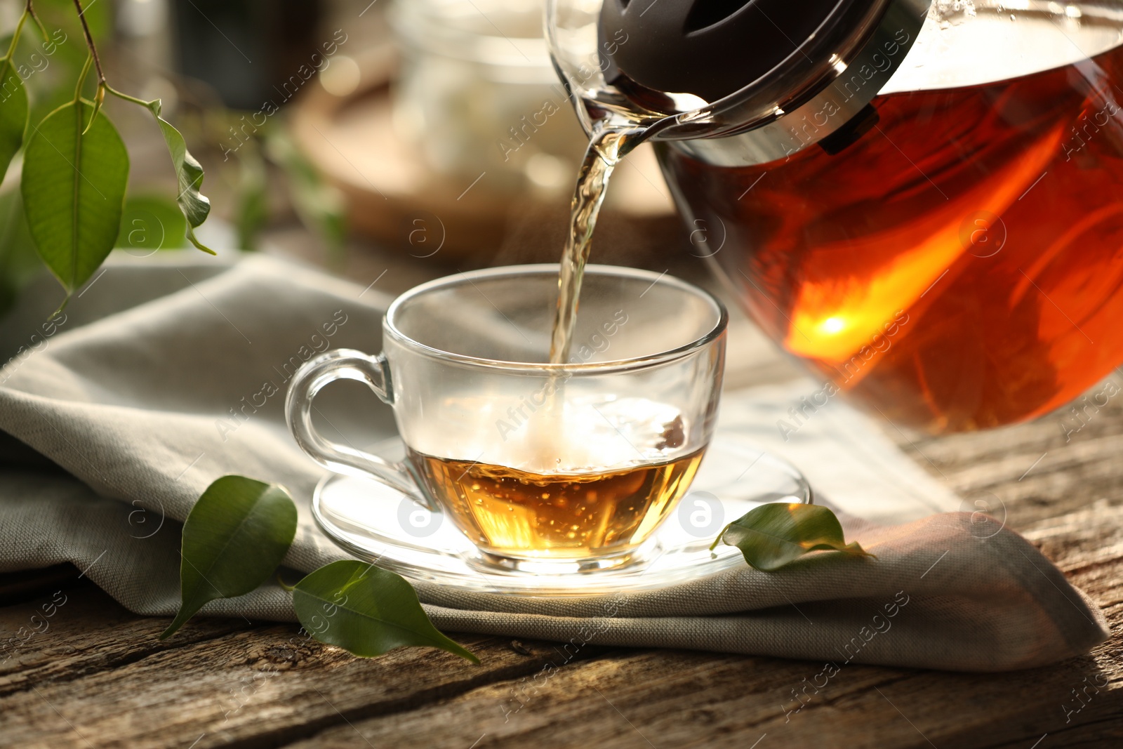 Photo of Pouring tea into cup on wooden table, closeup