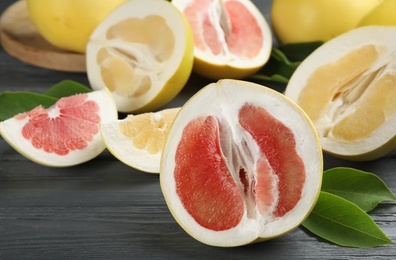 Photo of Fresh cut pomelo fruits with leaves on grey wooden table, closeup