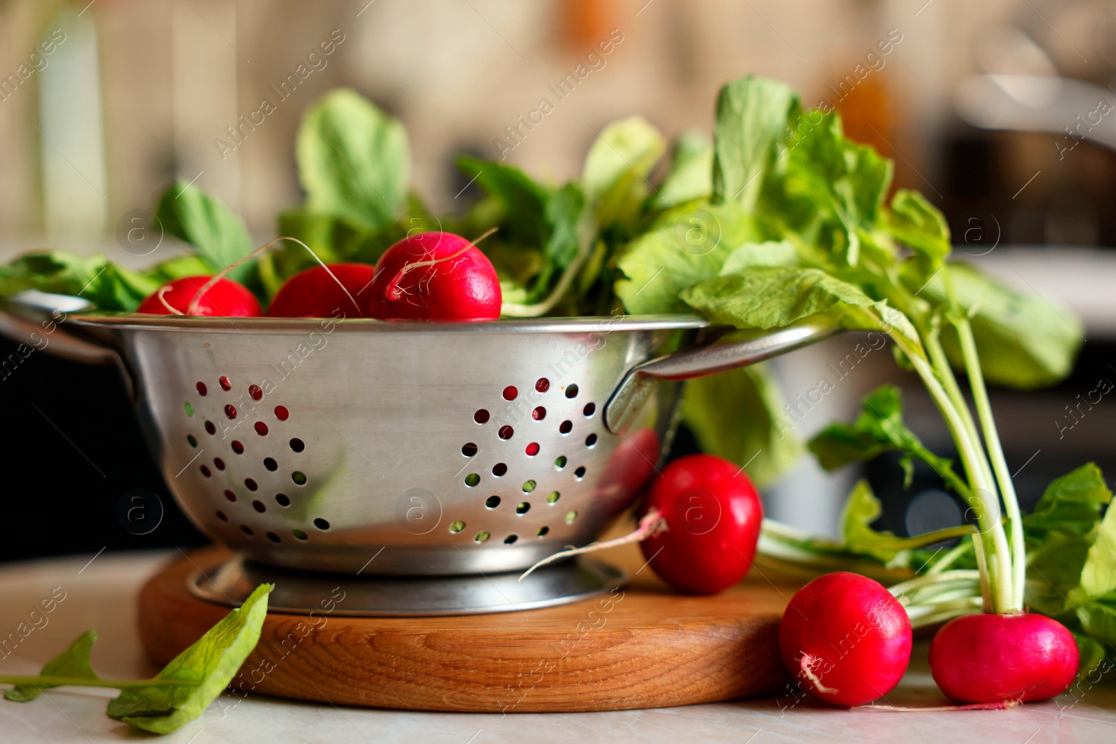 Photo of Metal colander with fresh radishes on white table, closeup