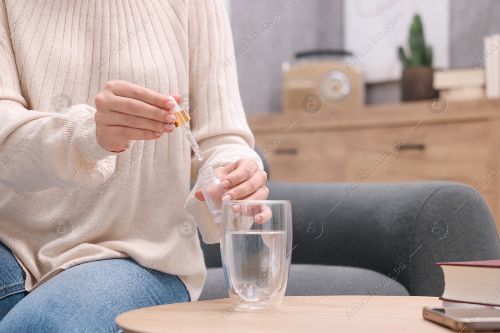 Photo of Woman dripping food supplement into glass of water on wooden table indoors, closeup. Space for text