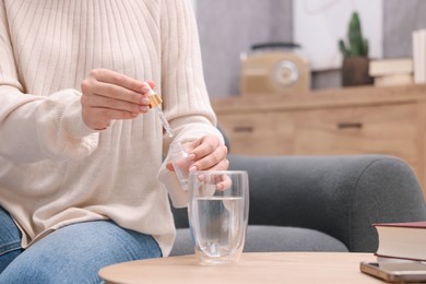 Woman dripping food supplement into glass of water on wooden table indoors, closeup. Space for text