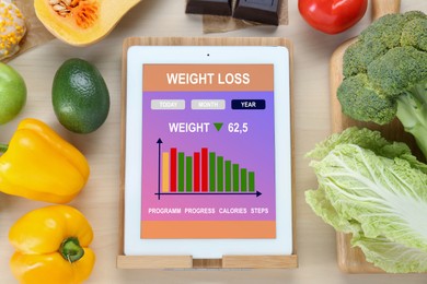 Tablet with weight loss calculator application and food products on wooden table, flat lay